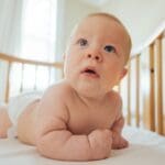 cute-baby-in-diaper-lying-on-wooden-crib-bed