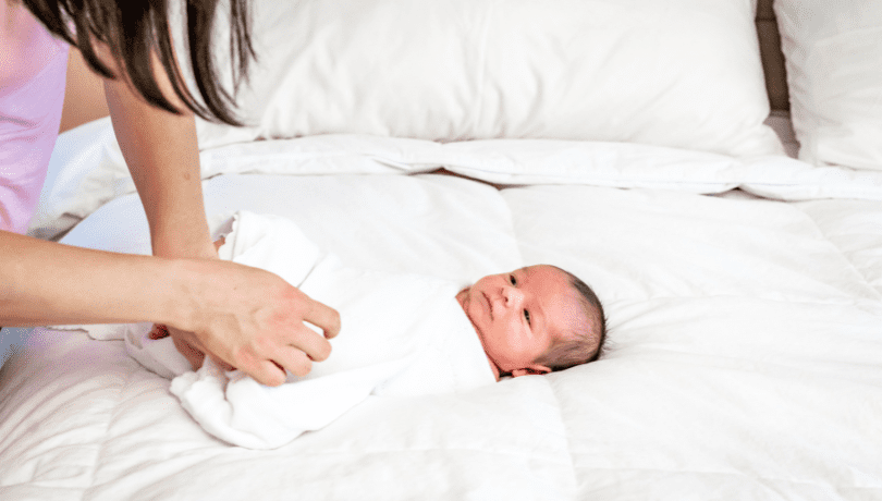 mother-swaddling-her-newborn-baby-with-a-white-swaddle-blanket
