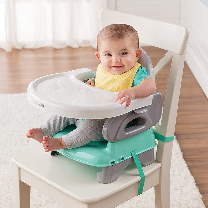 A toddler sitting in a gray table booster seat with safety straps
