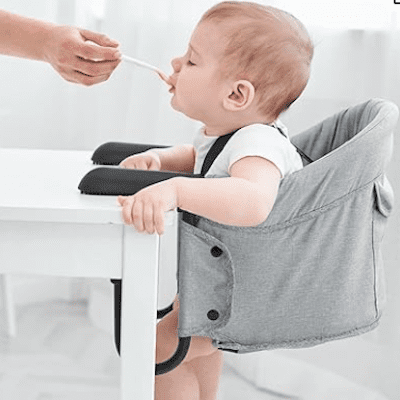 A baby sitting in a booster seat at the table, smiling and eating food